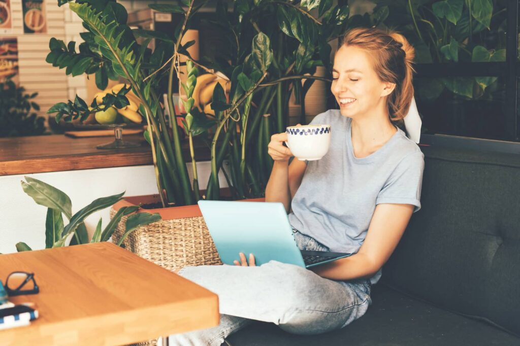 Girl smiling and drinking warm drink while looking at laptop.